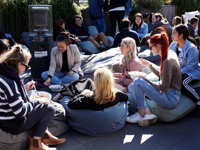 Group of Canva colleagues sitting on the rooftop at the Sydney office having lunch together