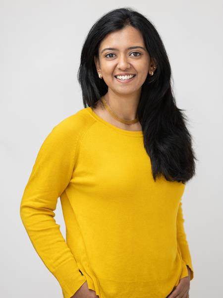 Woman with long black hair in a yellow shirt smiling to the camera