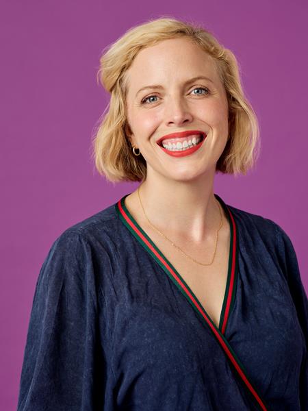 Light skinned woman in a blue dress and red lipstick, smiling.