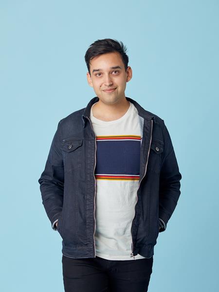 Man with hands in pocket smiling at camera wearing a denim jacket and striped t-shirt