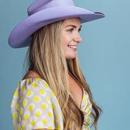 Women with blonde hair wearing a purple cowboy hat smiling into the distance