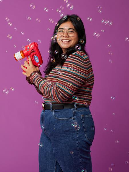 Women smiling tot he camera. She has a bubble machine and is making bubbles for the camera.