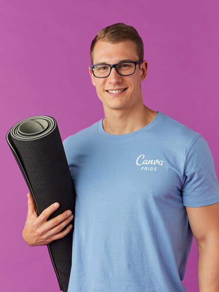 Light skinned man in blue t shirt with 'Canva' printed on it, holding a rolled up mat under his arm.