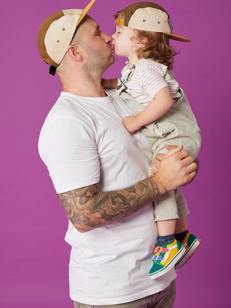 Light skinned man in white t shirt, jeans and a cap holding a small light skinned child and kissing him.