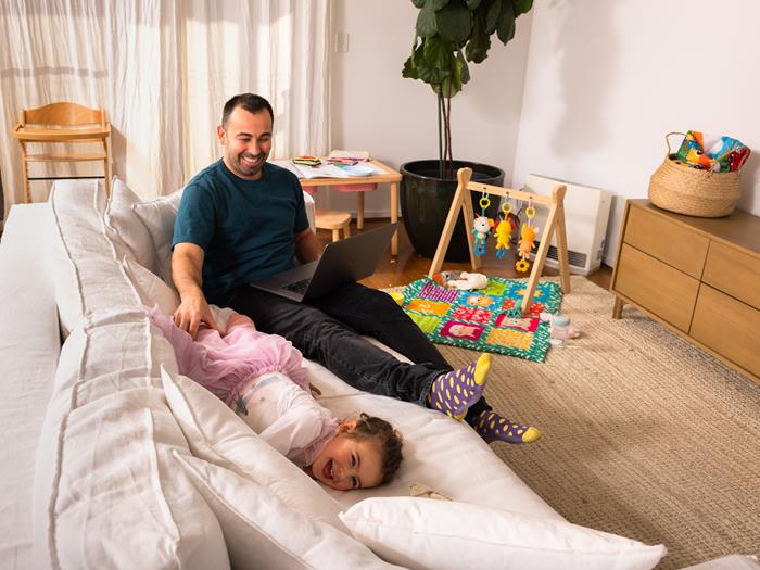 Father at home sitting on the lounge with his daughter tickling her. Both laughing
