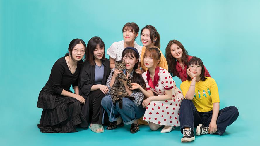 Groupd of women posing for a photo against a blue backdrop. One women holding a cat.