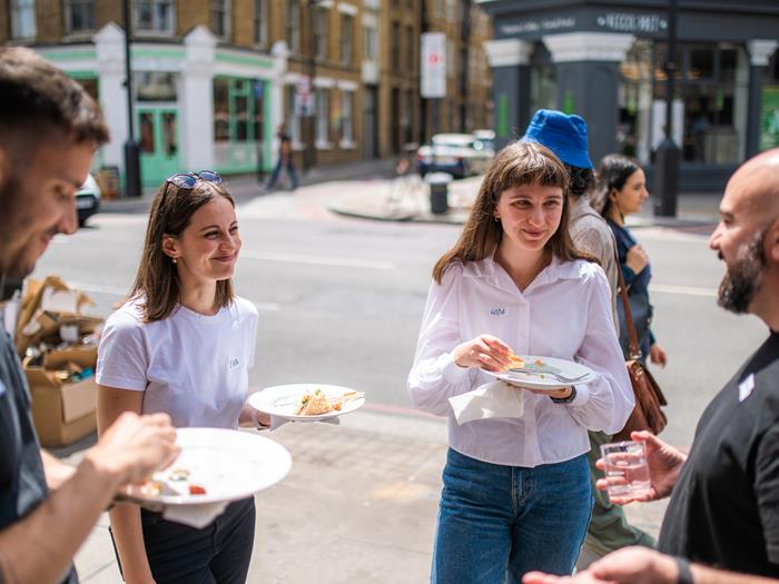 A group of colleagues out on the street in London talking to each other and holding plates of food