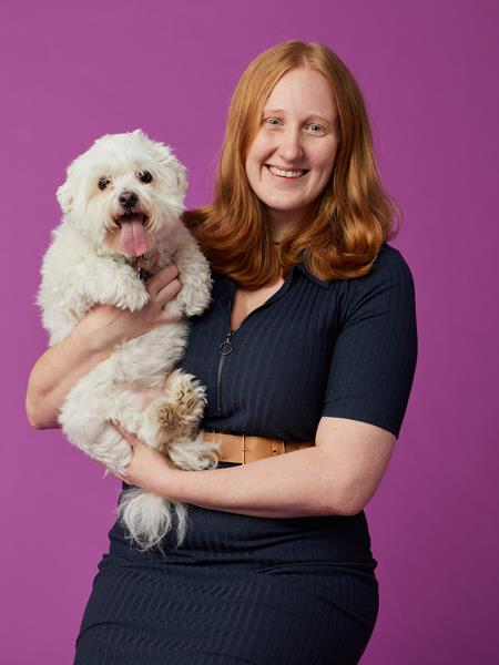 Women holding white fluffy dog and smiling front on at the camera