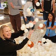 3 people sitting in a ball pit, throwing the balls in the air and laughing
