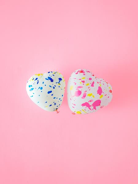 Two speckle love heart balloons together on a pink background.