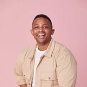 Man sitting on a chair with a pink background smiling at the camera