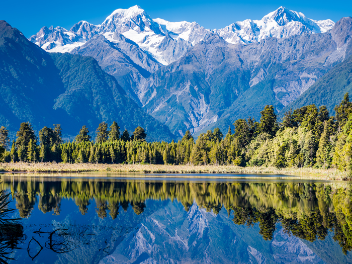 Mountains and trees with a crystal clear lake in the foreground.