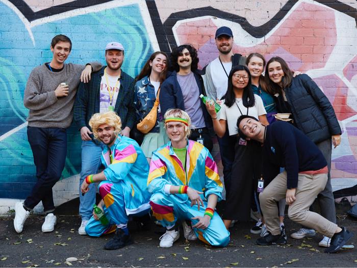 A group of people who work at Canva posing for a photo together in front of a coloured brick wall