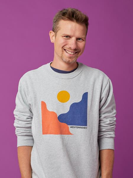 Light skinned man in grey sweatshirt, smiling.