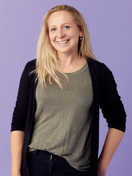 A light skinned woman in a grey t shirt and black cardigan, smiling.
