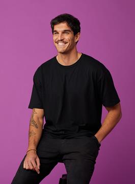 Man with a black t-shirt on, sitting on a chair smiling off to the distance