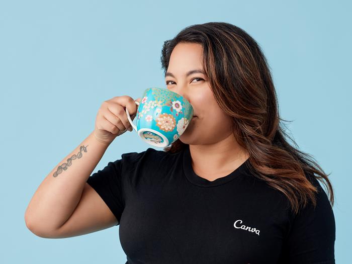 Medium skinned woman wearing jeans and a black t shirt holding a cup of tea.
