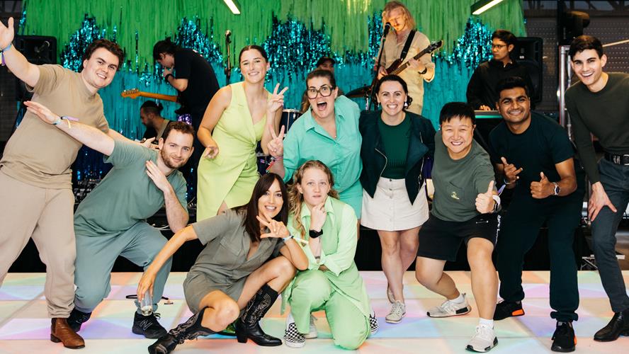 Group of people posing for a photo on a dance floor in front of a band playing on a stage.