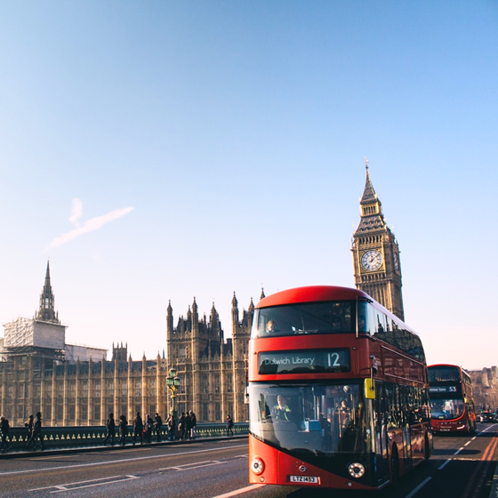 A red bus going over a London bridge with Big Ben in the background
