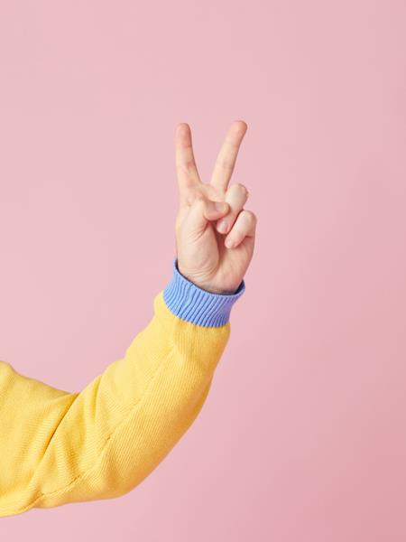 Person holding their hand up in a peace sign against a pink background
