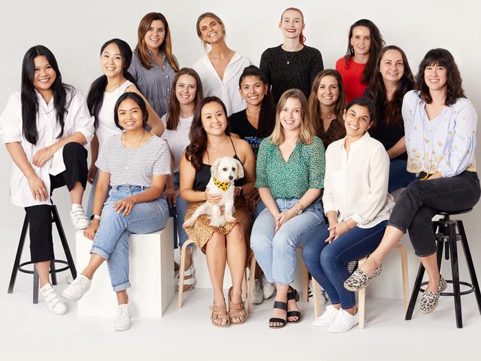 Canva's Operations team posing for a photo sitting on stools. One woman has a white dog on her lap.
