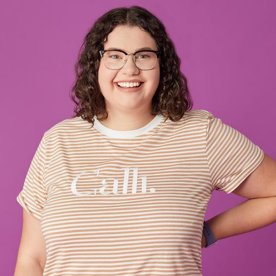 Women with curly brown hair and wearing glasses with a striped t-shirt. Smiling at the camera