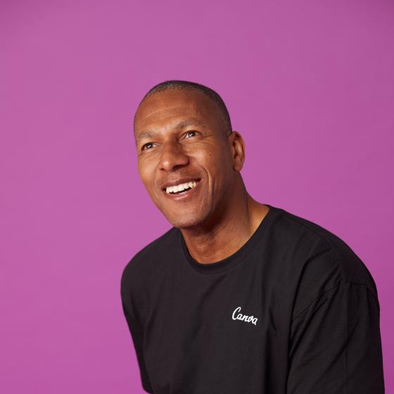 Man with a black t-shirt sitting on a stool smiling into the distance