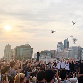 A bunch of people on a rooftop releasing doves into the sky