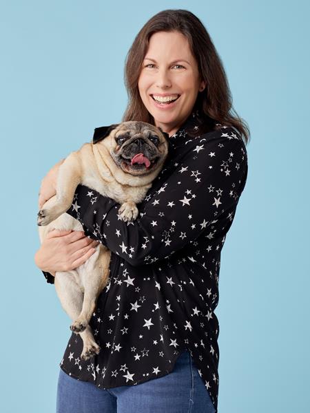 Light skinned woman in jeans and a star print shirt holding a pug.