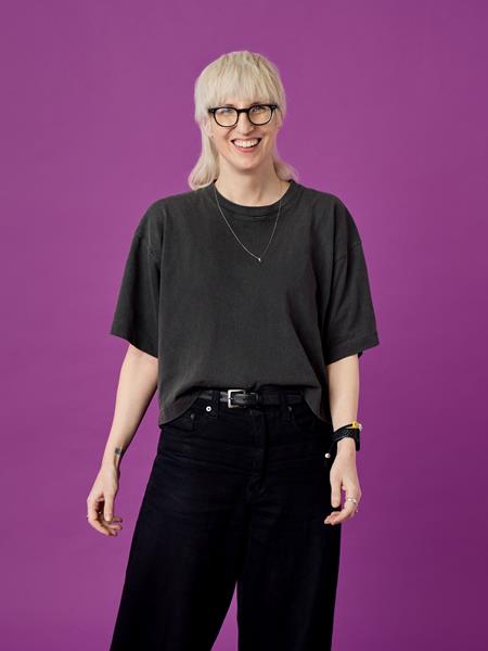 Light skinned woman in black trousers and t shirt, smiling.