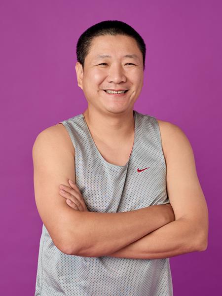 Medium skinned man in grey exercise singlet with his arms folded, smiling.
