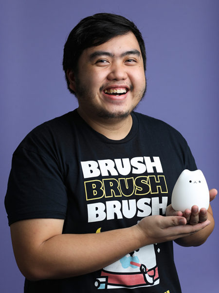 Medium skinned man wearing a black t-shirt holding a toy cat, smiling.