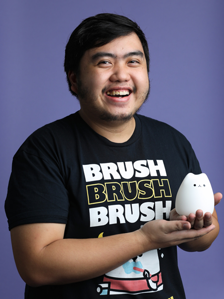 Man wearing a black t-shirt and smiling to the camera holding a cat prop