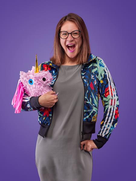 Women wearing a colourful jacket posing for a photo holding a unicorn paper mache