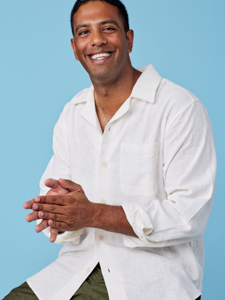 Dark skinned man in white shirt and green shorts, smiling.