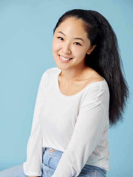 Medium skinned woman in white top and jeans, smiling.