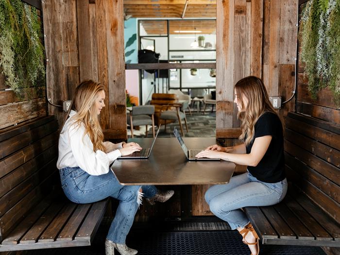 Two women on their laptops sitting in a booth working in the Austin office