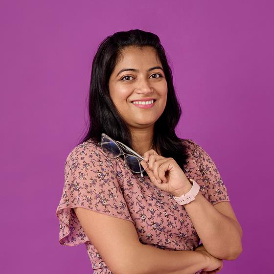 Medium skinned woman wearing a floral dress, holding a pair of glasses.
