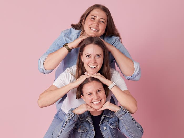 Three women standing in a row, resting their hands on their heads and smiling to the camera