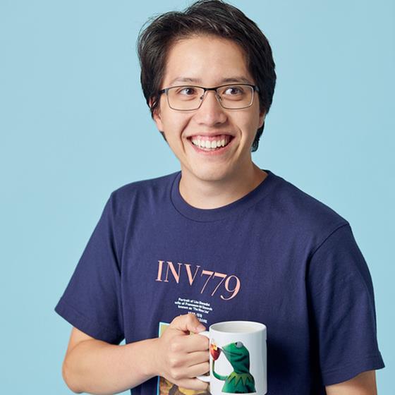 Man with black hair and glasses wearing a blue t-shirt smiling at the camera and holding a mug